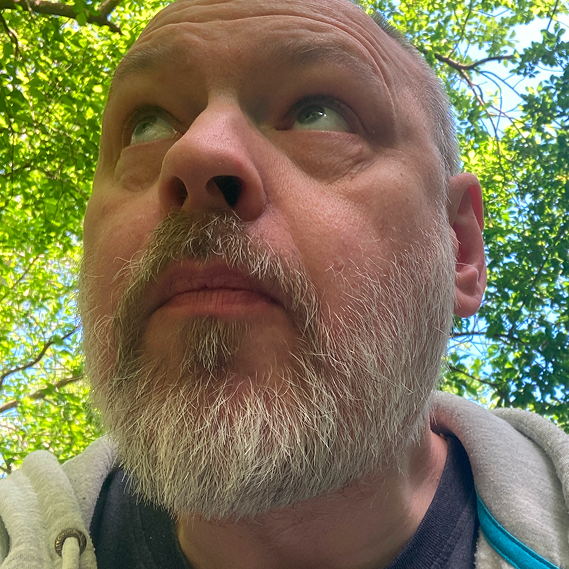 Biggs Thorarensen, a full-bearded white male looking up at the sky with trees in the background